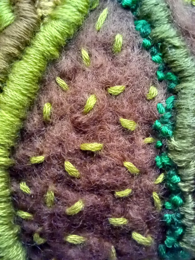 green embroidery thread used for a seed stitch on a brown roving.
